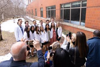 Students standing in white coats outside posing for photos.
